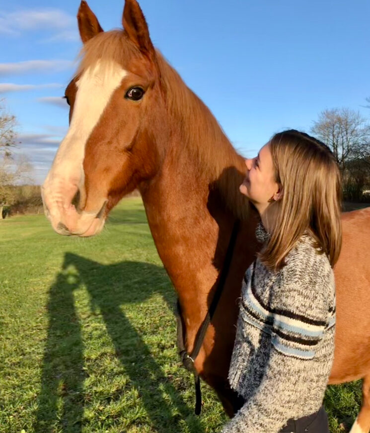 La psychologue, Hanna, avec un cheval qui a marqué son parcours de vie en liberté dans une prairie. On y voit le bonheur et le bien-être qu'on peut ressentir grâce au cheval.