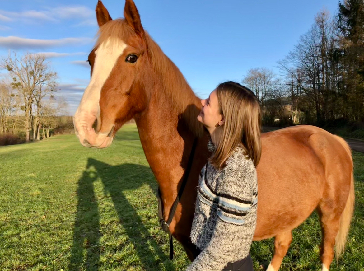 La psychologue, Hanna, avec un cheval qui a marqué son parcours de vie en liberté dans une prairie. On y voit le bonheur et le bien-être qu'on peut ressentir grâce au cheval.